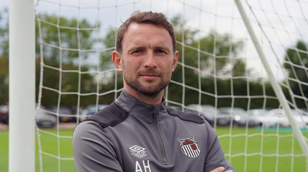 Alex Hughes posing for a picture while stood in a goal wearing a Grimsby Town tracksuit.