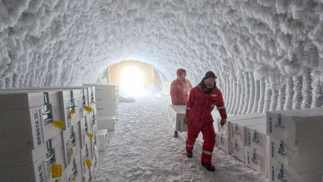 Two scientists moving a box with ice inside a frozen cave.