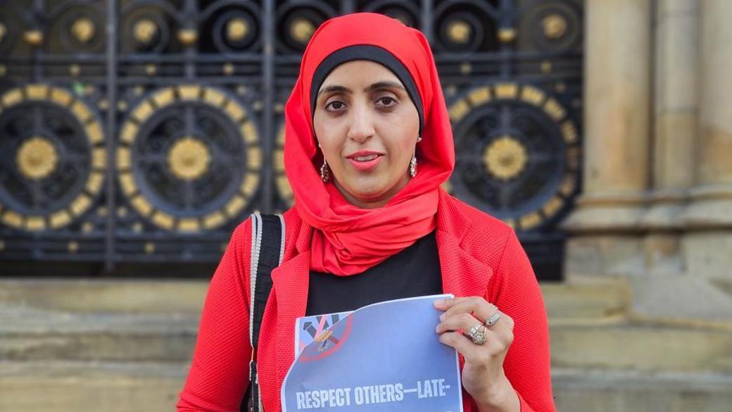 Councillor Fozia Shaheen stands in front of Bradford City Hall holding a document titled, "Respect others - late-night fireworks"