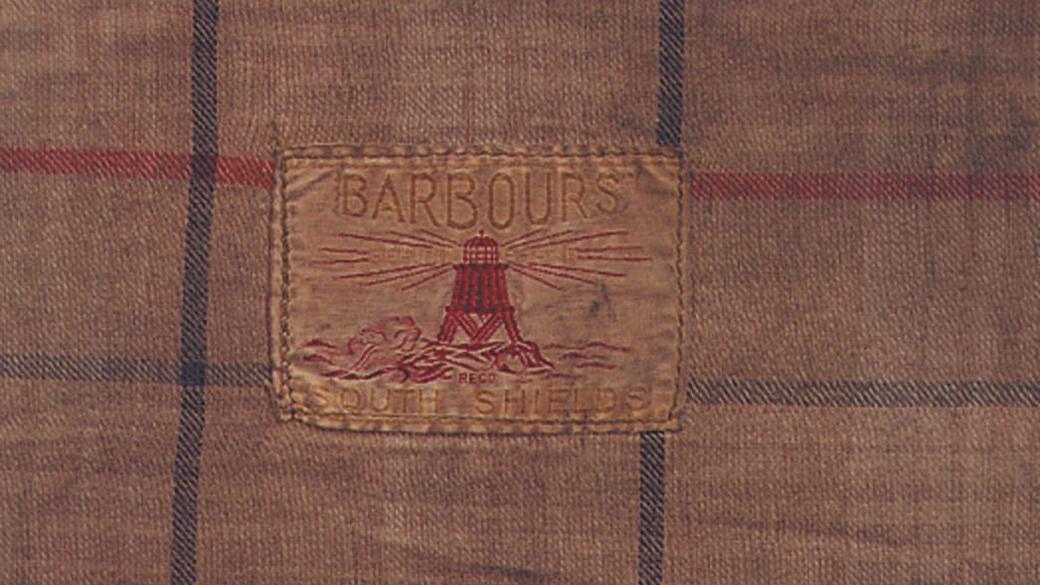 A piece of checked fabric bearing Barbour's South Shields emblem, depicting the Herd Groyne lighthouse 