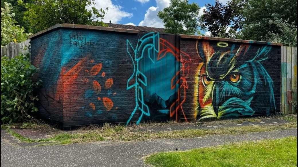 Blue and orange and yellow owl painted on a garden wall 