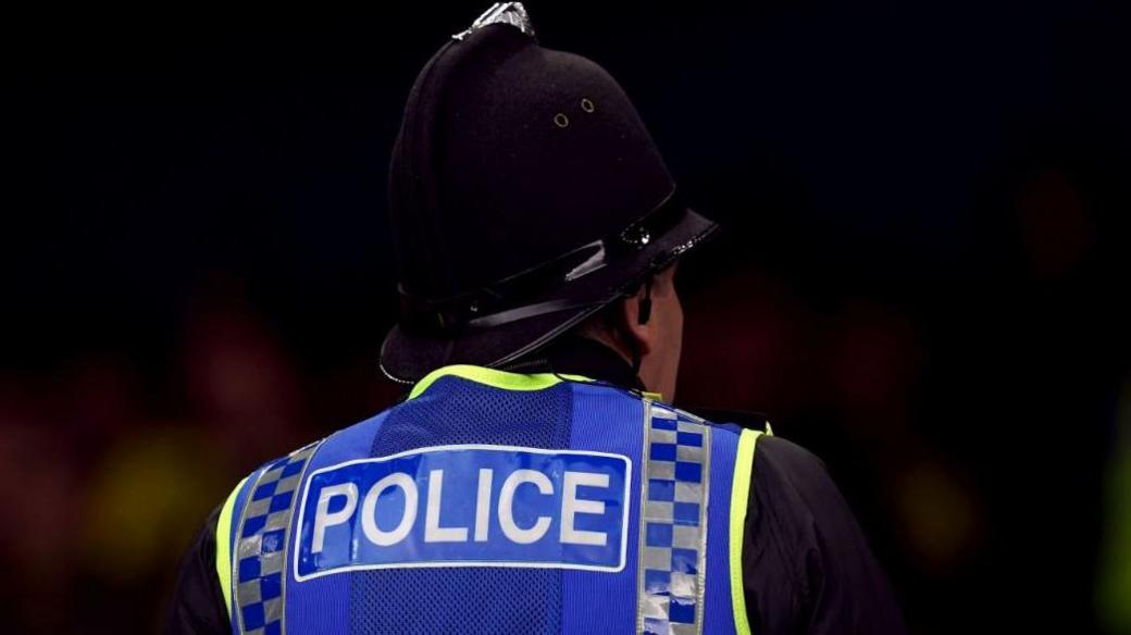 The back of a police officer, who is wearing a helmet and a high-vis jacket that says POLICE.