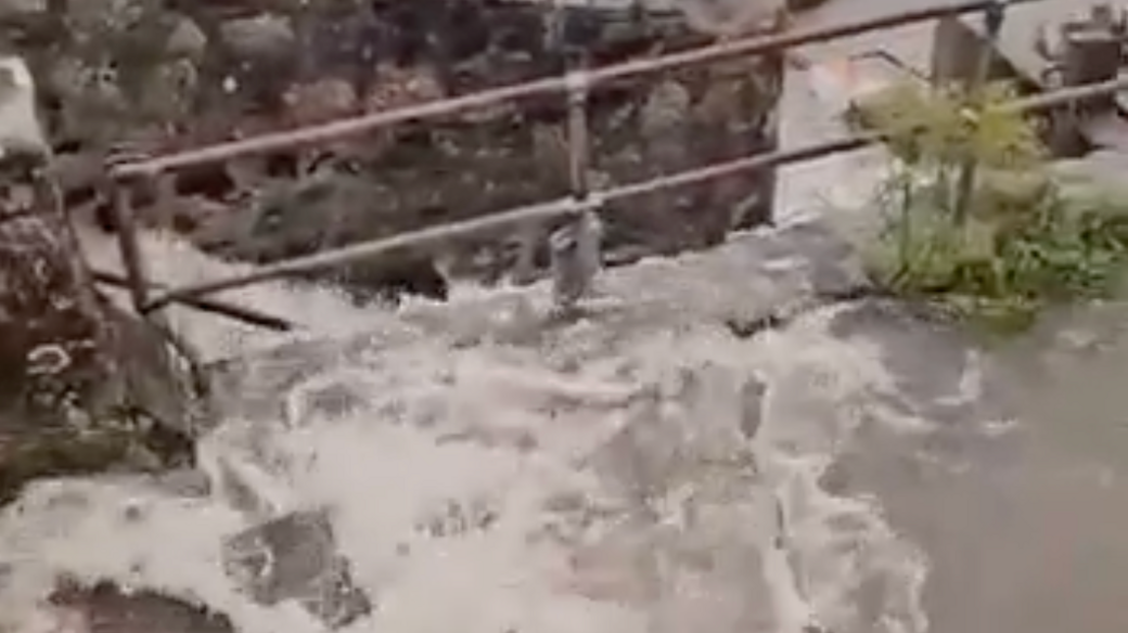 Water flowing down a concrete staircase in St Ives, Cornwall. There is a metal railing and a brick wall.