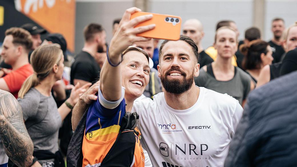 Woman standing next to Mike holding a phone up while taking a selfie. They are in a crowd of people