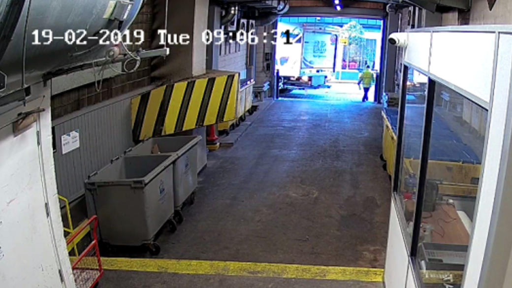 A man wearing a hi-vis jacket directs the driver of an HGV which is reversing into a loading and unloading bay.