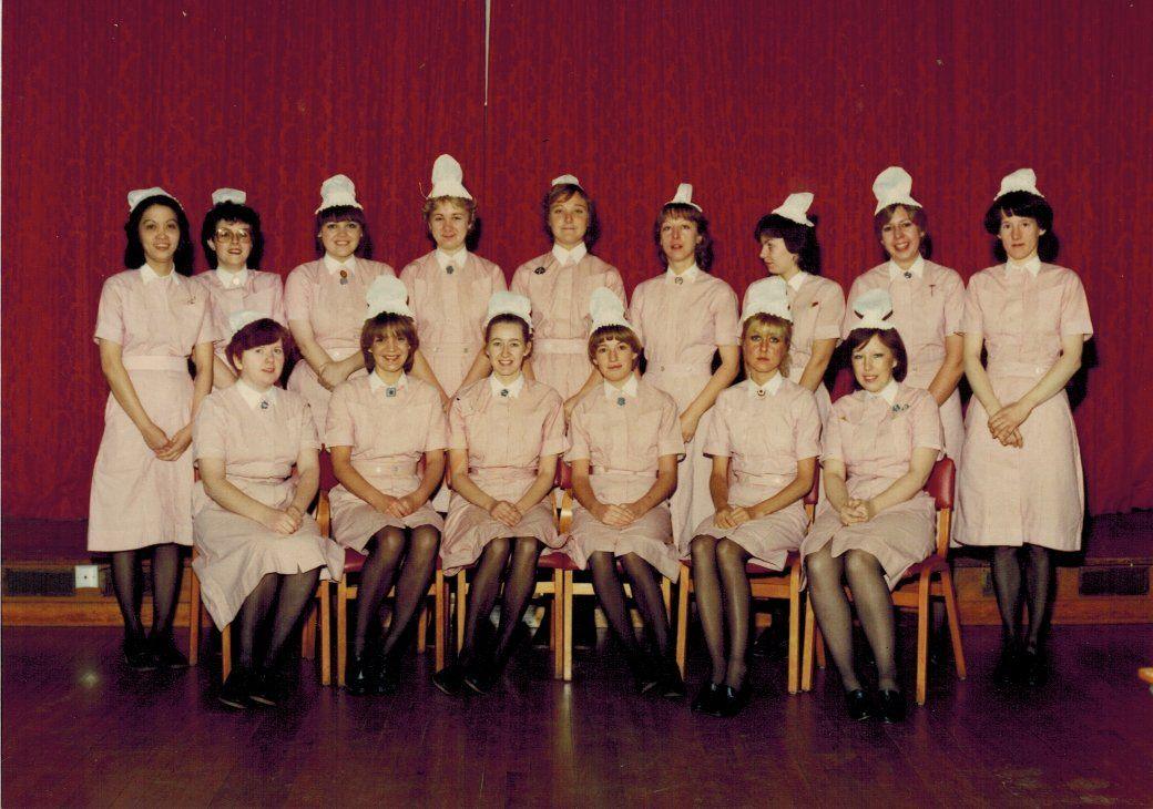 Fifteen women in pink uniforms with white hats and collars pose for a photograph in two rows. 