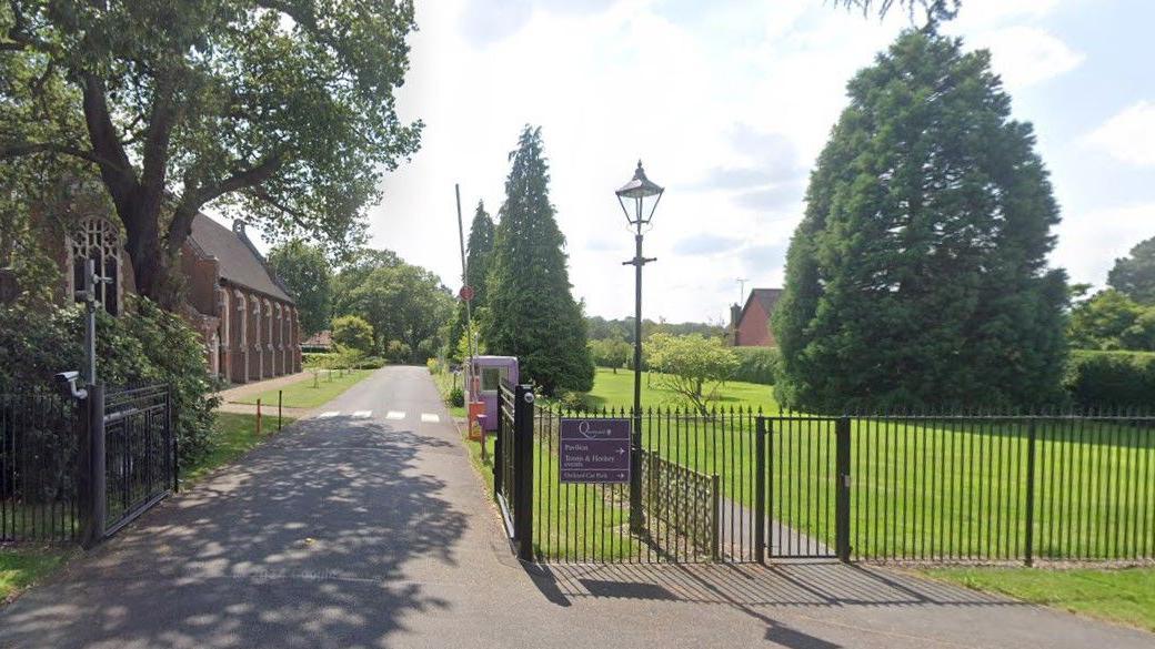 Part of the grounds of Queenswood. There is a gated entrance, and ornate building and a large tree on a lawn