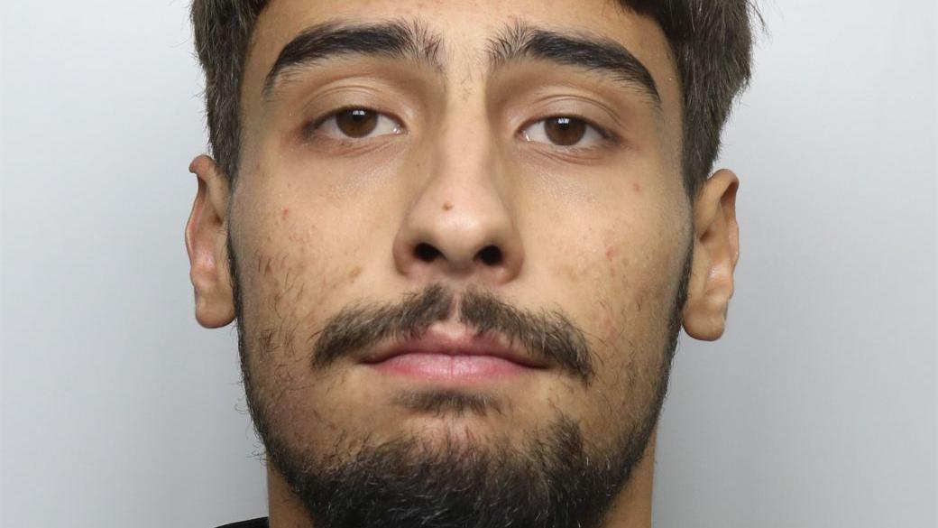 A custody photo of a man with brown eyes, short brown hair and facial hair
