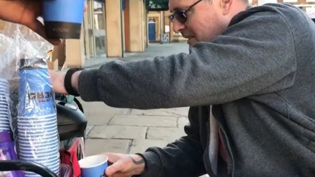 A man in a black sweater and glasses pouring coffee into a cup 