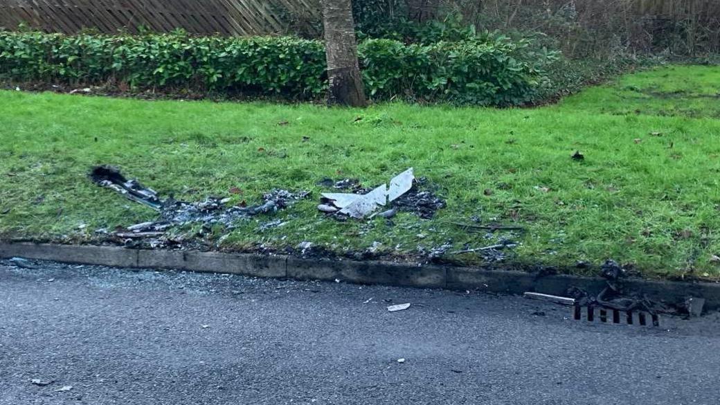 An image of discarded parts of the burned out bus on roadside and on a bit of grass on a verge.