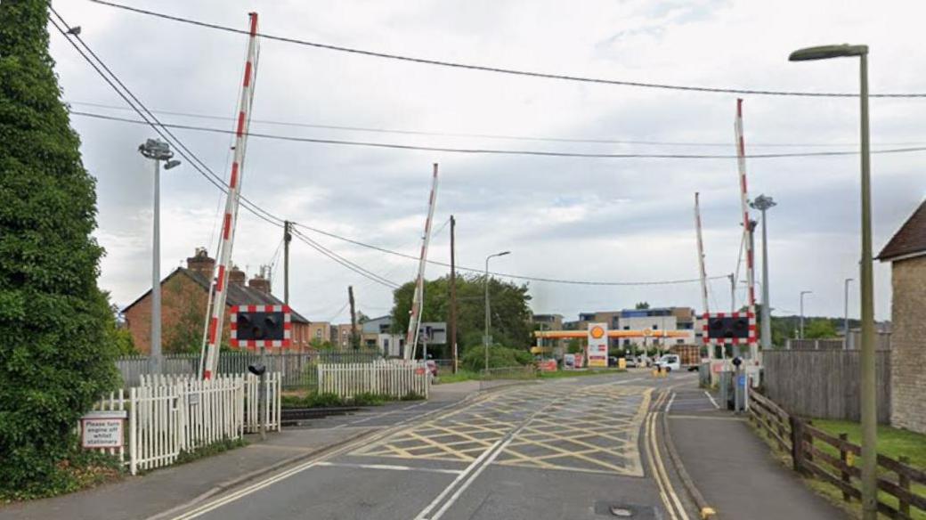 A google maps screenshot of the london road rail crossing. It is on a single carriageway, and has four separate barriers, as well as lights. Further down the road is a petrol station.