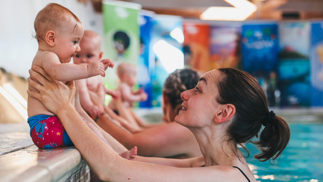 A mother in a swimming pool holding her baby on the side