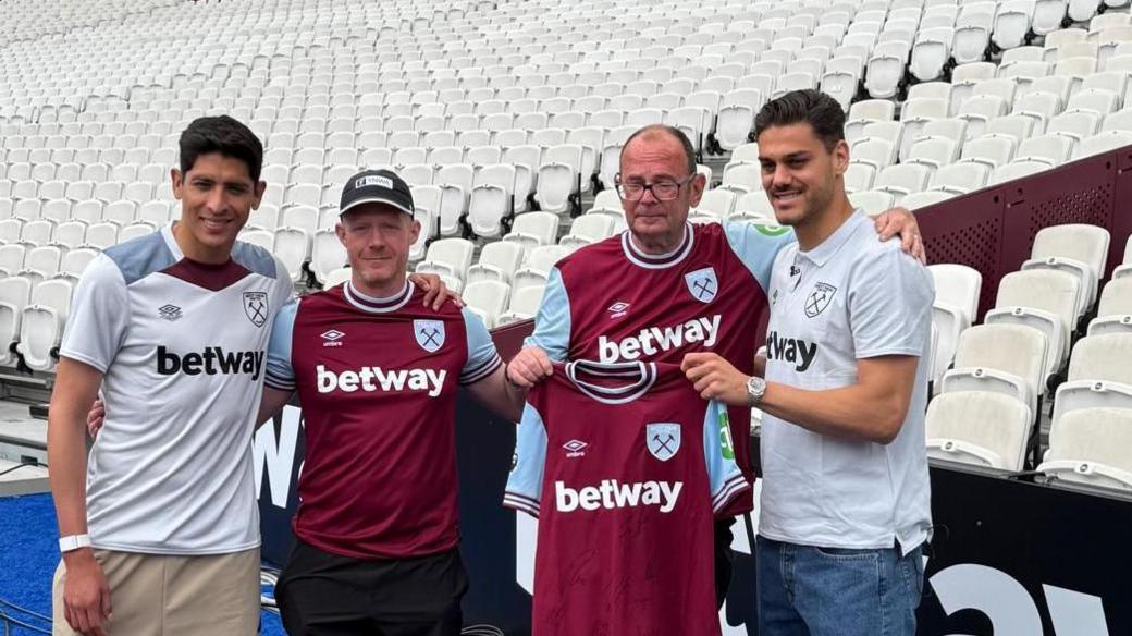 Richard and Martin standing with a signed West Ham shirt presented by Edson Alvarez and Konstantinos Mavropanos pitchside at the London Stadium