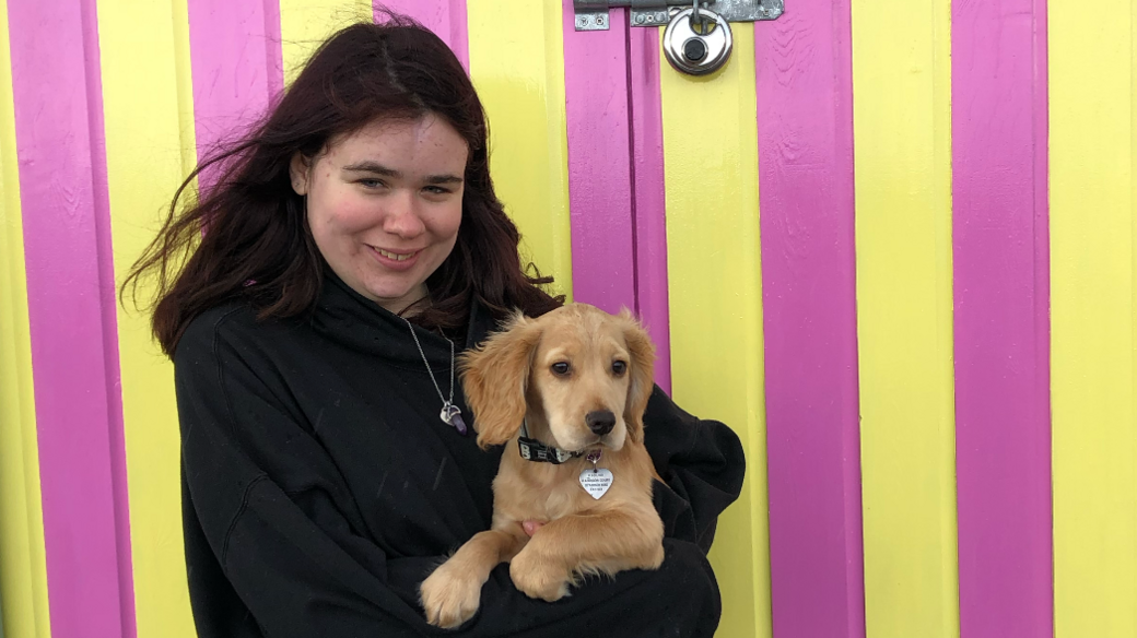 Hannah standing with her puppy in front of a beach hut 