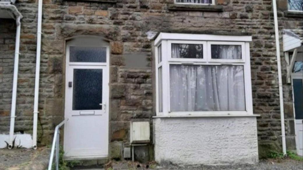 A brick terraced house that has been donated to The Wallich. It has a white door and a white bay window still. 