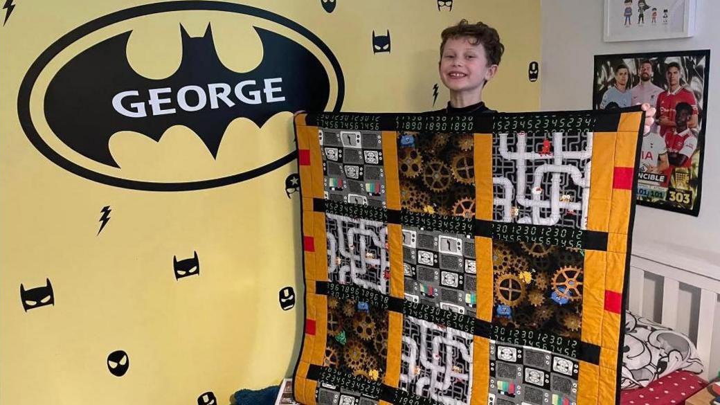 George in his room, standing on his bed, holding a quilt