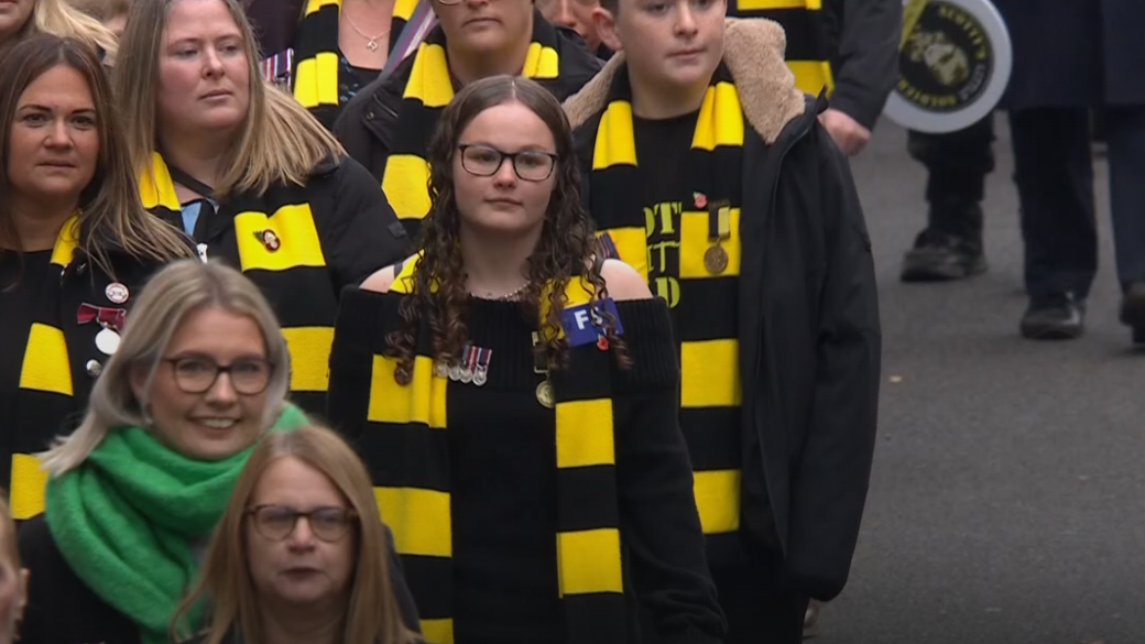 Adults and young people wear black and young scarves as they walk down Whitehall