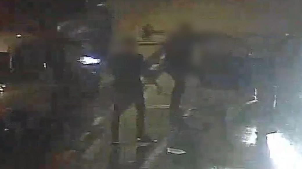 CCTV still with blurred close-up of two men in a confrontation on the road at night.