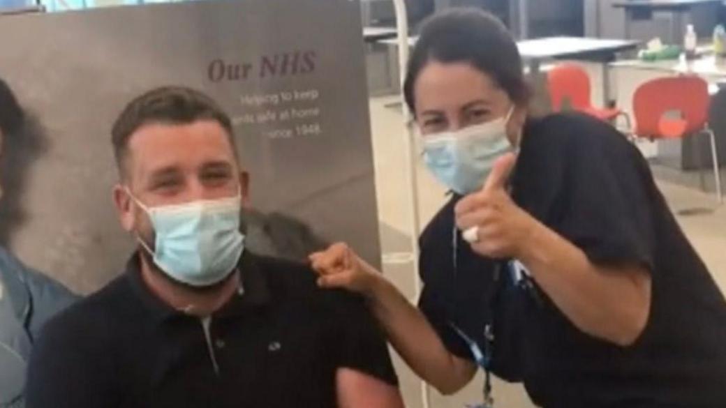 Jo Downs giving a thumbs up to the camera alongside  a member of the public. Both of them are wearing masks.