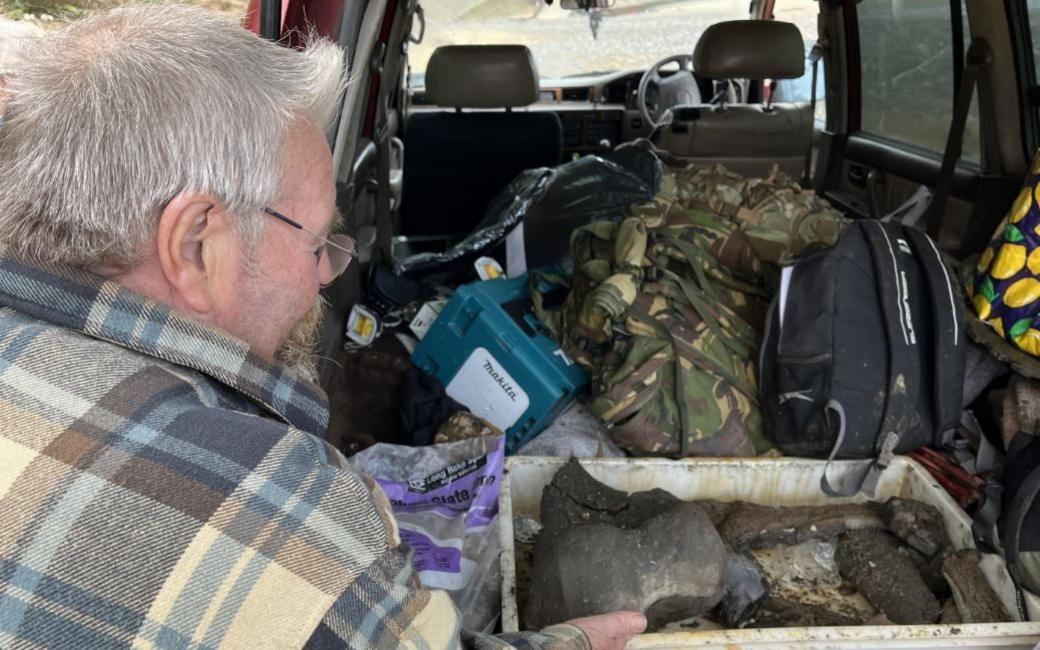 John Clayden, wearing a thermal tartan shirt, reaches into the open car boot to hold a bone