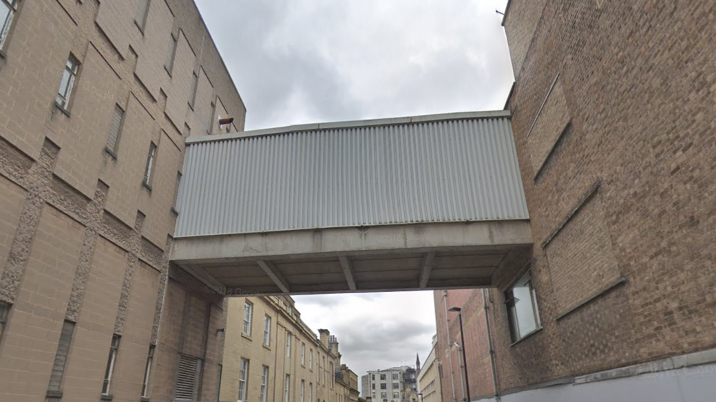 A concrete bridge links two sand-coloured buildings