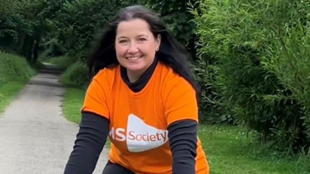 Woman on a bike on the Camel Trail at Wenford Bridge wearing a bright orange multiple sclerosis t-shirt