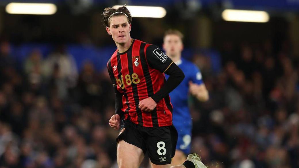 Alex Scott running in his black and red striped Bournemouth kit while playing away at Chelsea