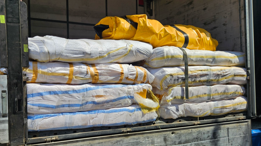 Eight, white rolled-up items in the back of a lorry. There is what looks like a deflated, yellow boat on top.