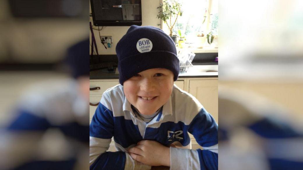 A young boy in a blue beanie hat. He is smiling.