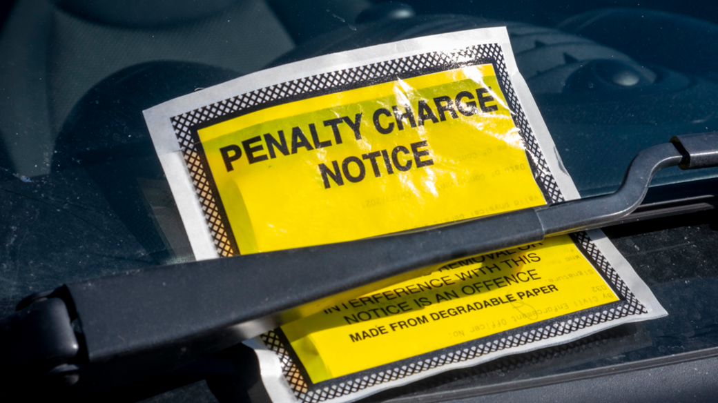 A yellow penalty charge notice underneath a car windscreen wiper