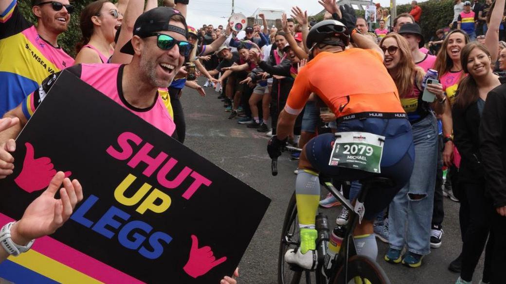 Members of Swansea and Vale Triathlon Club cheering on cyclists with signs at Heartbreak Hill. 