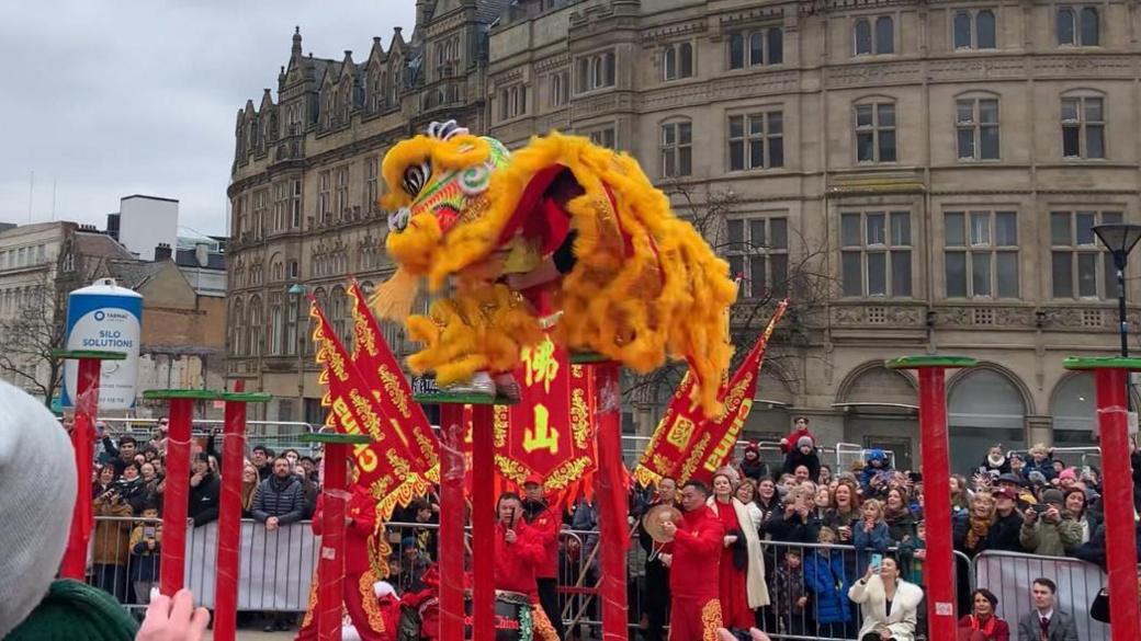 A yellow and gold dragon puppet parades over red and green poles in Sheffield City Centre