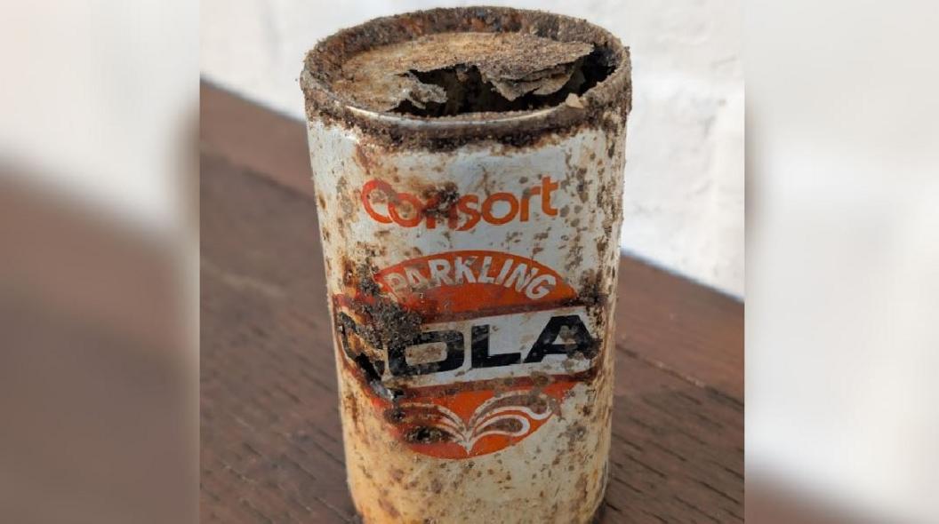 An extremely rusty old Consort cola can. It has orange writing and an orange circle in the middle with "Cola" written in black across it. 