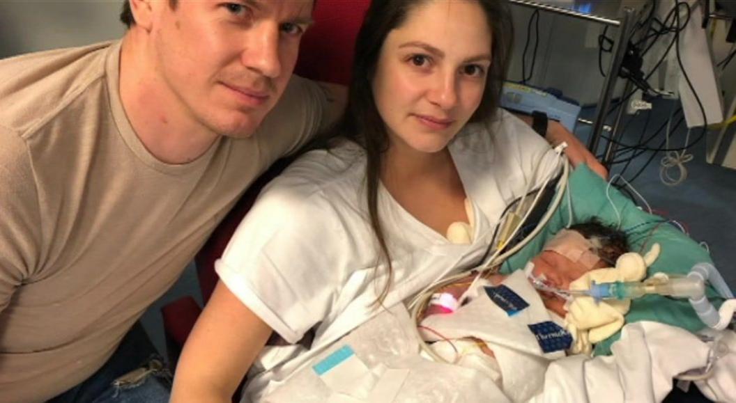 A man and a woman cradle a newborn baby in a hospital bed. The baby is connected to an ventilator and other emergency equipment. 