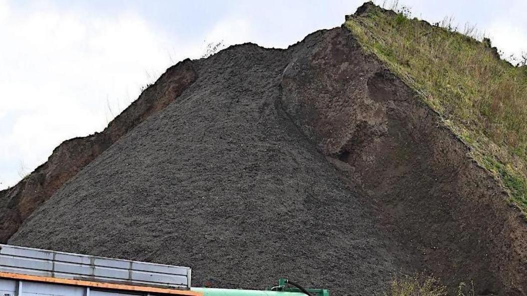 A large mound of waste buried in a landfill covered with soil and grass 