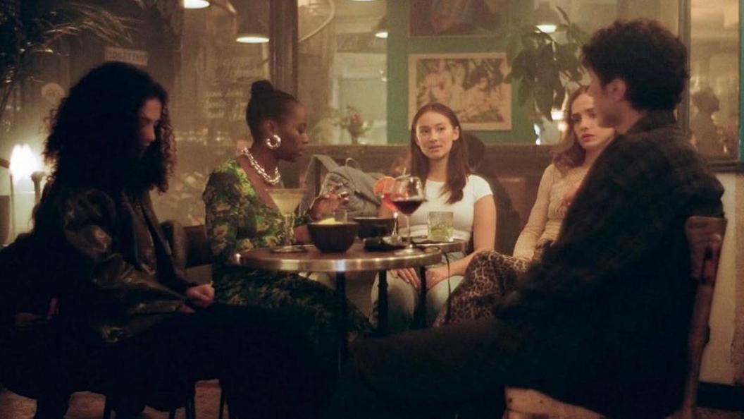 A scene from The Summer I Turned Pretty - cast members sit around a table in a bar with drinks laid out