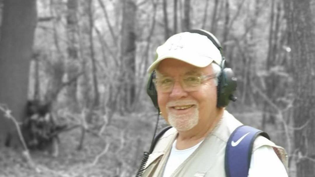 An elderly man with earphones on and a Nike backpack. 