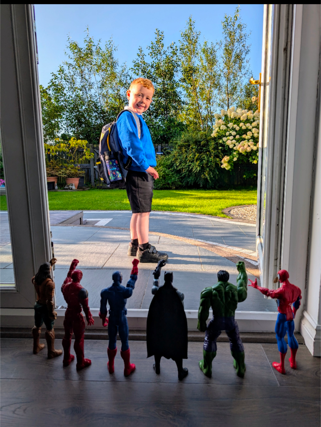 Young child in a school uniform, looking back to an open door smiling at some action figurine toys posed as though waving at him