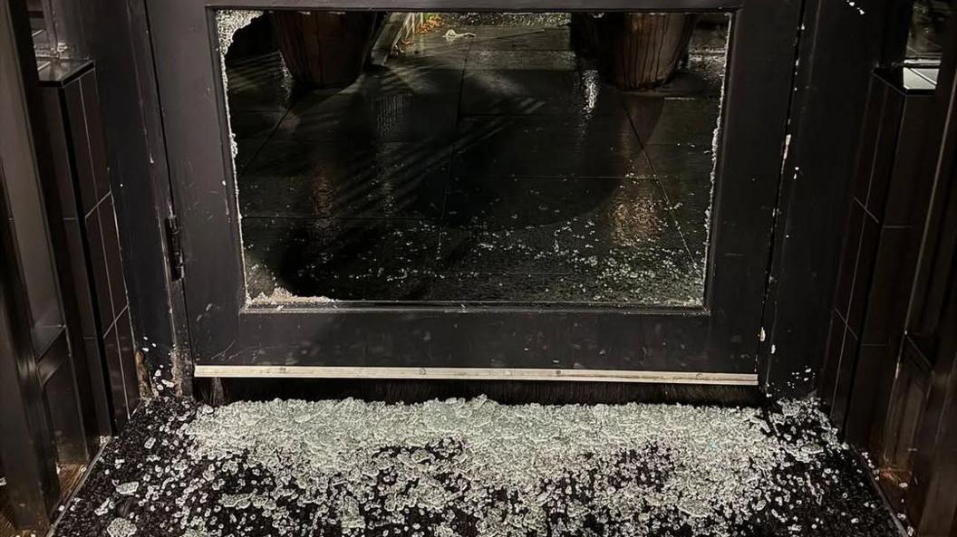 Llun o ddrws blaen y bwyty wedi'i chwalu a gwydr dros y llawr.