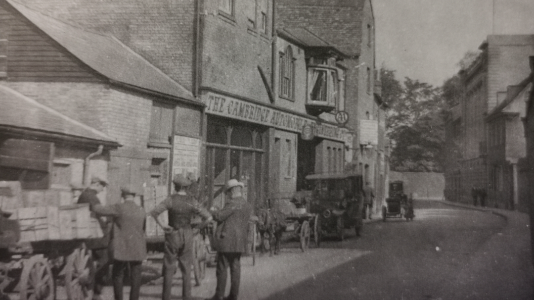 Black and white photo of 21 Hobson Street as the Cambridge Automobile Engineering company, a group of men are standing on the street next to a cart