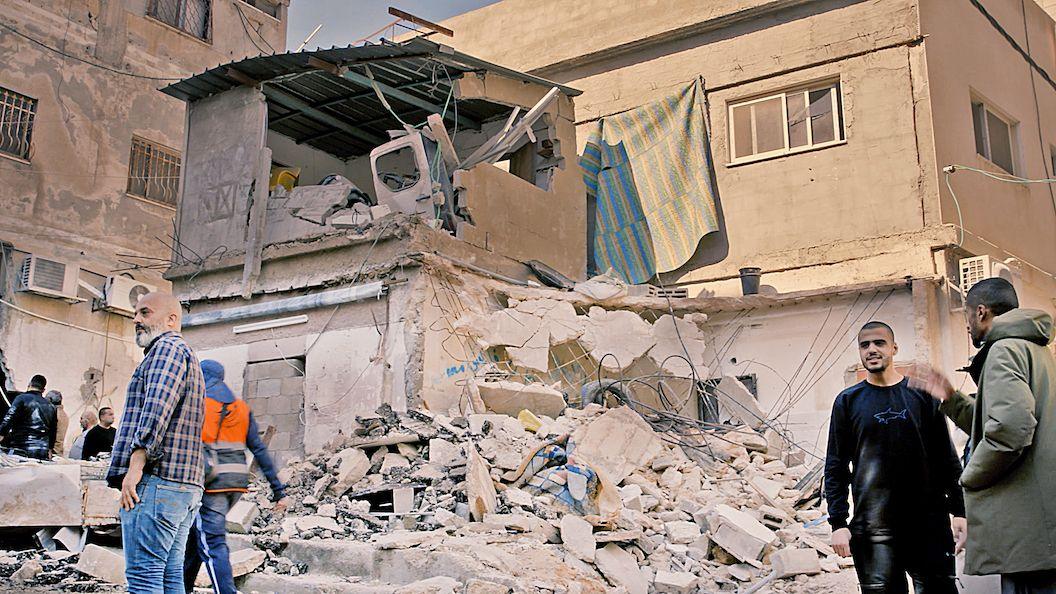 Palestinian men stand around amid the rubble of a concrete building 