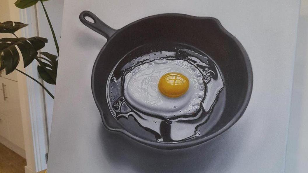 An oil painting of a fried egg in a black skillet. The egg looks in the process of being fried, there are no brown edges yet, only some air bubbles on the right corner as it sits in a sheen of oil.