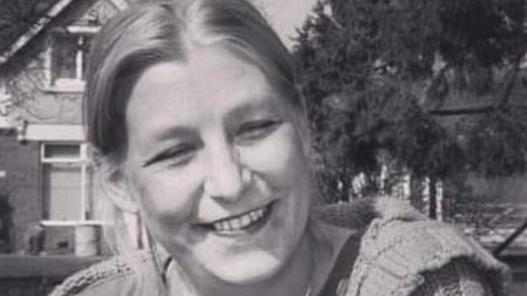 A black and white image of a woman with her hair in a pony tail wearing a woolly jumper. 