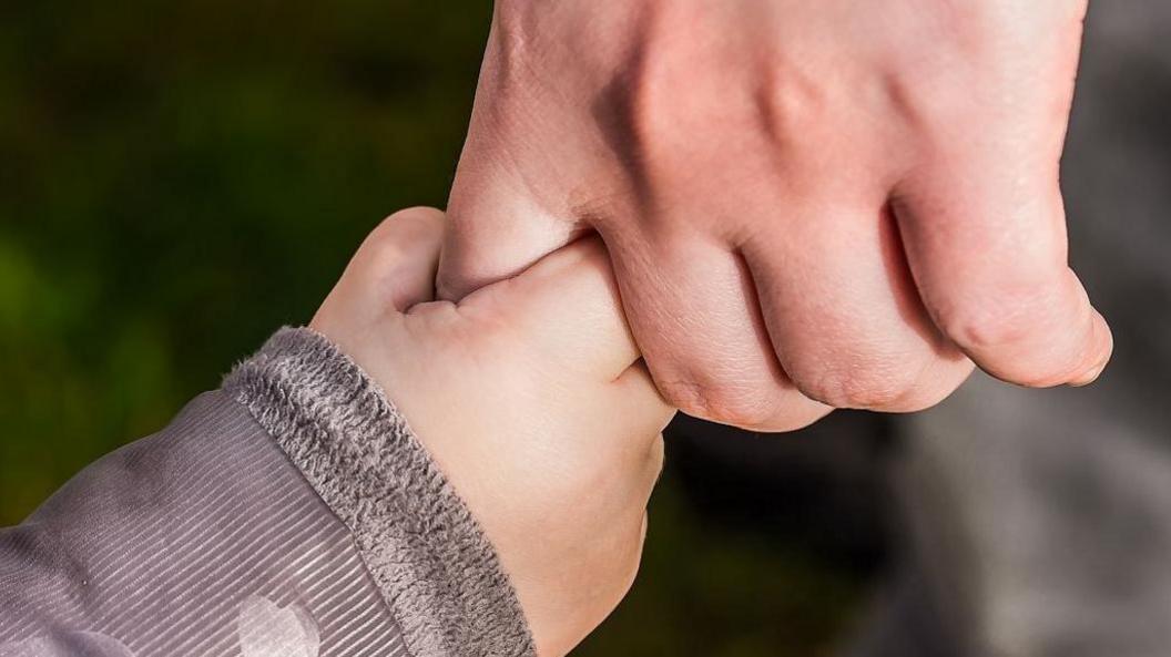 Man holding child's hand. The child's arm is in a grey coat.