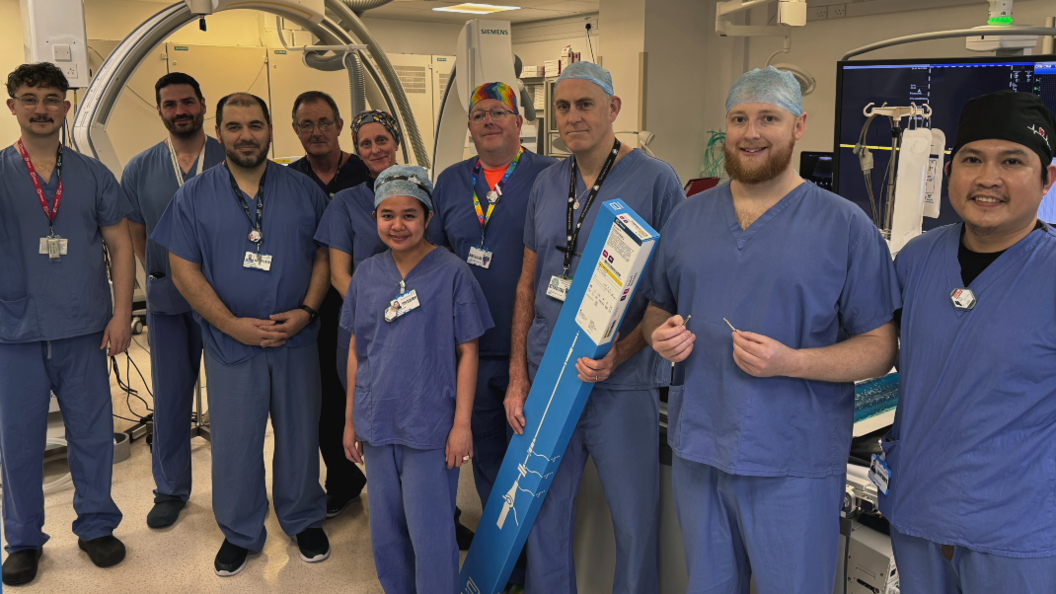 Ten people in surgical scrubs uniform in an operating theatre. One holding a long box which contains the tube used to insert the pacemakers. 