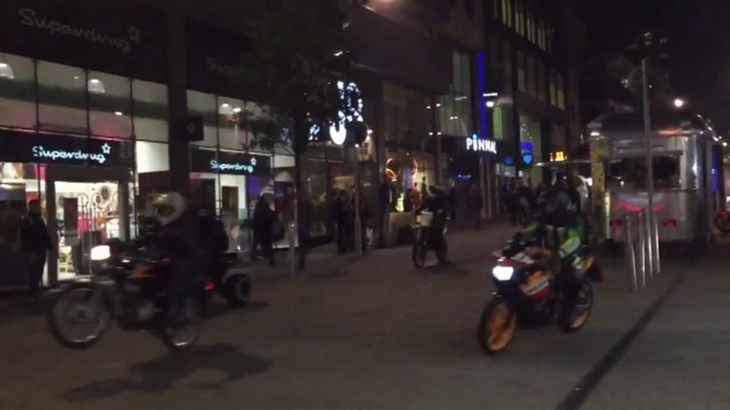 Bikers riding on a pavement with one on the left doing a wheelie