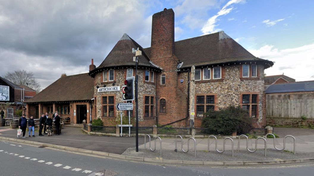 Google street view image of the Artichoke pub where people are stood outside and walking past. 