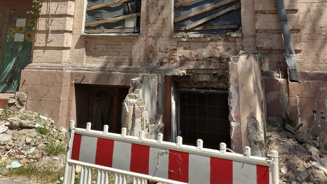 A no entry barrier is up in front of a building that has been damaged and there's rubble in front of the building.