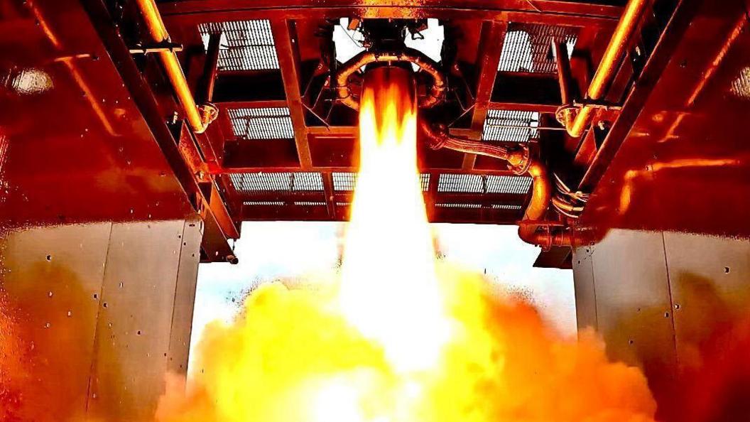 The bottom of a rocket engine firing flames and smoke into a chamber. 