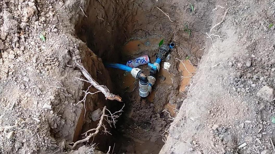 A excavated hole shows a connection between two water pipes at a property's boundary.